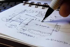 las manos del arquitecto dibujan planos arquitectónicos con lápices en un cuaderno de bocetos en un escritorio con una computadora portátil. foto
