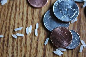 las monedas de dólar y los billetes de dólar están esparcidos sobre una mesa de madera con granos de arroz. foto