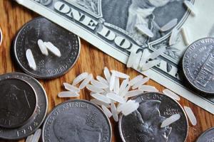 Dollar coins and dollar bills are scattered on a wooden table with grains of rice. photo