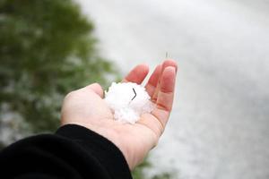 A man's hand holding snow in his hand after it snows against a snow-covered road in the background. photo