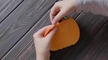 Women's hands are sweeping a decorative pumpkin from felt. Cozy autumn decorations made of felt for the home. Decorative pumpkins for Halloween. video