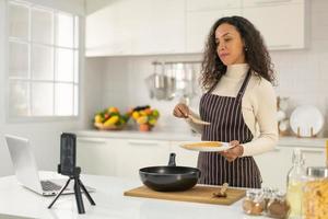 mujer latina grabando video y cocinando en la cocina foto
