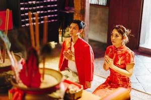 feliz joven pareja asiática con vestidos tradicionales chinos rezando en el templo foto