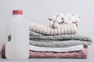 wool detergent in a bottle and stack of pullovers with cotton buds. special fabric softener for delicate textile and knitted apparel photo