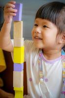 una niña jugando con bloques de madera en la habitación. niña usando bloques de madera coloridos crea torres y la construcción mejora la habilidad motora fina de los niños. divertidos juegos educativos para el concepto de niños. foto