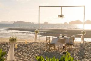 Beautiful table set up for a romantic dinner on the beach with  flowers and candles. Catering for a romantic date, wedding or honeymoon background. Sunset beach dinner. selected focus. photo