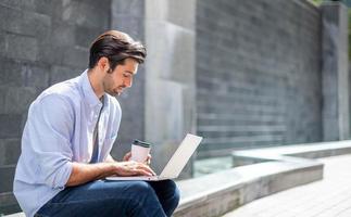 Young caucasian man sitting and working on freelance project using portable computer at outer office. photo