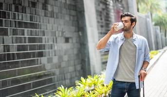 Young caucasian man drinking coffee and pulling the suitcase waiting his friend for travel together. photo