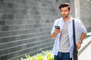 The business man using a smart phone on their way. Feeling happy and relaxing, Casual young businessman wearing suit jacket and shoulder bag. photo