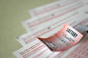 Red lottery ticket lies on pink gambling sheets with numbers for marking to play lottery. Lottery playing concept or gambling addiction. Close up photo