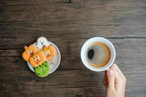 hand holding coffee cup during eating funny Halloween Cookies. Happy Halloween day, Trick or Threat, Hello October, fall autumn, Traditional, party and holiday concept photo