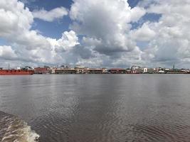 el ancho río donde pasan los barcos con vistas de nubes blancas y cielos azules y en el medio hay edificios de mercado tradicionales alineados foto