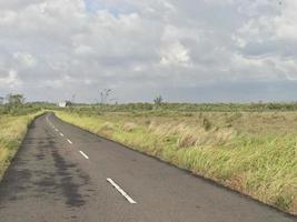 The view of the highway with beautiful grass stretching along the edge of the road and white clouds covering photo