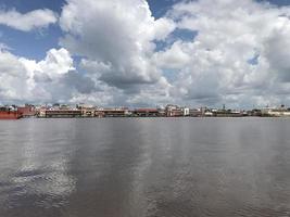 el ancho río donde pasan los barcos con vistas de nubes blancas y cielos azules y en el medio hay edificios de mercado tradicionales alineados foto
