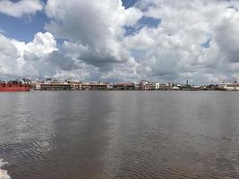 el ancho río donde pasan los barcos con vistas de nubes blancas y cielos azules y en el medio hay edificios de mercado tradicionales alineados foto