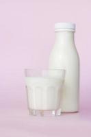 A bottle and a glass of white milk, highlighted on a pink background, close-up. photo