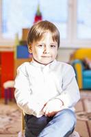 elegantemente vestido con una camisa blanca, un niño pequeño está sentado en el aula para recibir lecciones. retrato de un niño foto