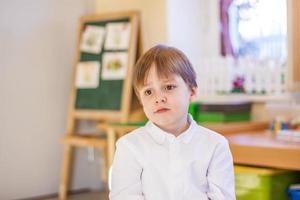 elegantemente vestido con una camisa blanca, un niño pequeño está sentado en el aula para recibir lecciones. retrato de un niño foto
