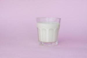 A glass of white milk, highlighted on a pink background, close-up. photo