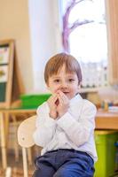 elegantemente vestido con una camisa blanca, un niño pequeño está sentado en el aula para recibir lecciones. retrato de un niño foto