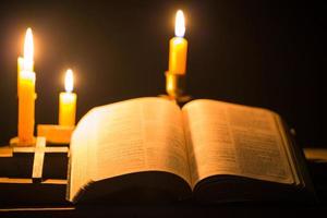 velas encendidas con la sagrada biblia y la cruz o el crucifijo sobre un fondo de madera antiguo en la iglesia. luz de las velas y libro abierto sobre una mesa de madera vintage estudio y lectura del cristianismo en el hogar. concepto de la religión de cristo foto