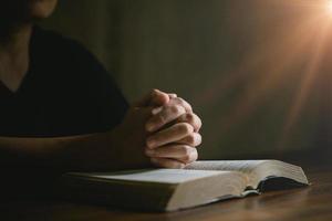 mano de persona de oración en fondo negro. la mujer católica cristiana está rezando a dios en la oscuridad en la iglesia. chica cree y fe en jesucristo. la religión de cristo y el cristianismo adoran o rezan concepto. foto