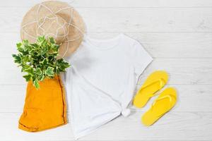 White closeup t shirt mock up flat lay and flip flops on white wooden background. Top view and copy space. Mockup summer t-shirt and summertime. Template blank shirt. photo