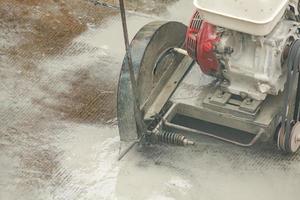 Worker using diamond saw blade machine cutting concrete road at construction site photo