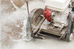 Worker using diamond saw blade machine cutting concrete road at construction site photo