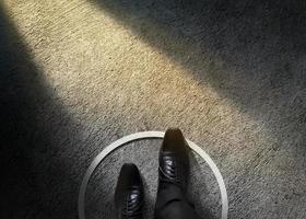 concepto de zona de confort. hombre de negocios con zapatos formales pasa por encima de la línea circular hacia fuera del límite blanco. vista superior, tono oscuro, sombreado claro en piso de cemento foto