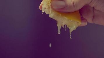 Hand squeezing half of lemon with lime drop on black background. video