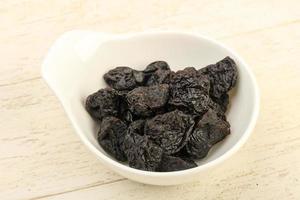 Dried plums in a bowl on wooden background photo