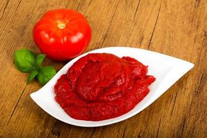 Tomato paste in a bowl on wooden background photo