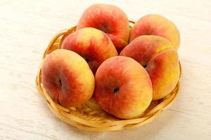 Sweet peaches in a basket on wooden background photo