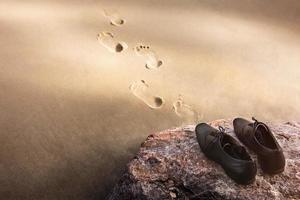 Work Life Balance Concept, Businessman take off his Working Oxford Shoes and leave it on the Beach Rock for Walk into the Sea in Sunny Day. Footprint on Sand. Top View photo