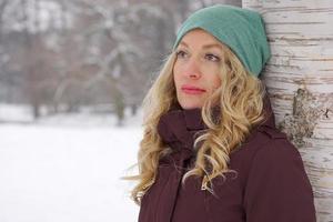 pensive woman leaning against tree in winter photo