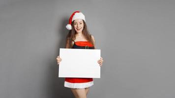 young woman in santa claus christmas costume presenting blank sign with copy space photo
