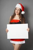 young woman dressed in christmas costume and santa hat presenting blank sign with copy space photo