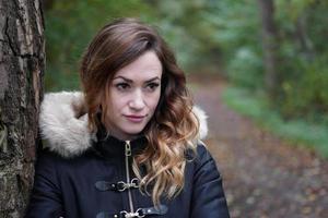 pensive young woman leaning against tree in forest photo