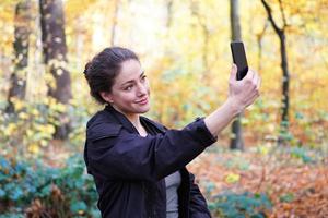 young woman taking selfie with smartphone in forest photo