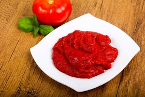 Tomato paste on the plate and wooden background photo