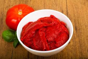 Tomato paste in a bowl on wooden background photo