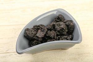 Dried plums in a bowl on wooden background photo