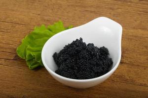 caviar negro en un recipiente sobre fondo de madera foto