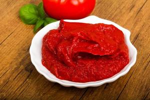 Tomato paste in a bowl on wooden background photo