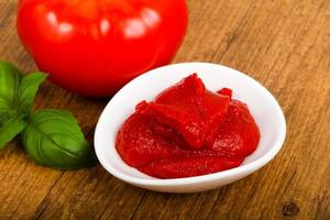 Tomato paste in a bowl on wooden background photo