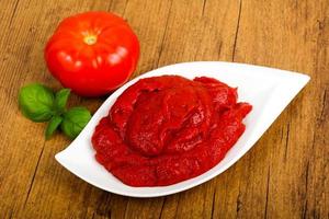 Tomato paste in a bowl on wooden background photo