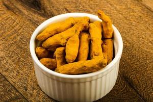Tumeric roots in a bowl on wooden background photo