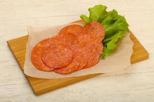 Pepperoni sausage on wooden board and wooden background photo