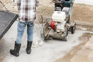 trabajador que utiliza una máquina de hoja de sierra de diamante cortando una carretera de hormigón en el sitio de construcción foto